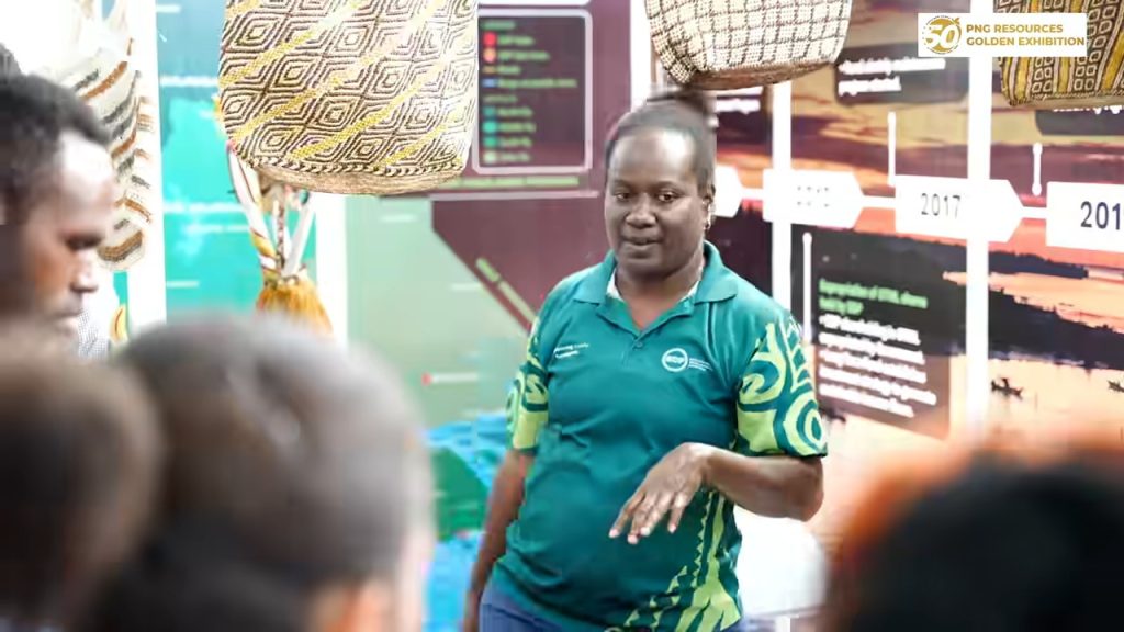 An exhibitor speaks with visitors beside woven bags at the PNG Resources Golden Exhibition