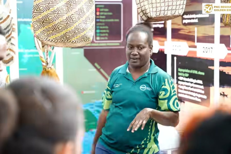 An exhibitor speaks with visitors beside woven bags at the PNG Resources Golden Exhibition